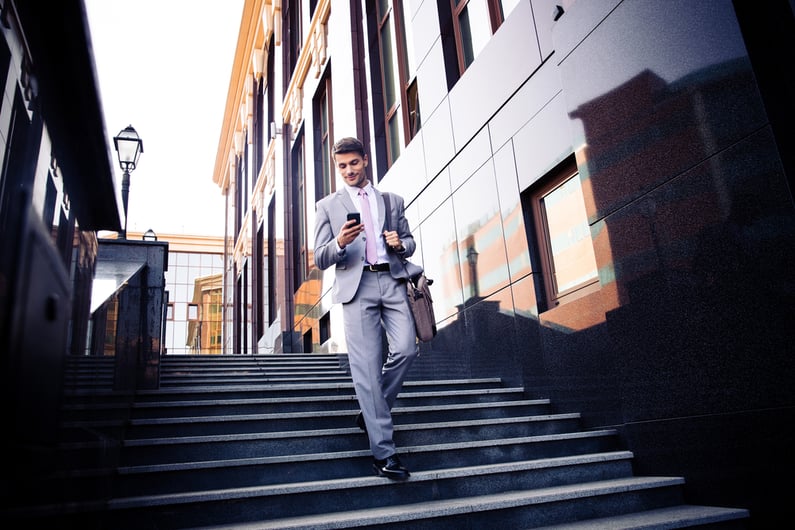 Happy businessman walking on the stairs and using smartphone outdoors