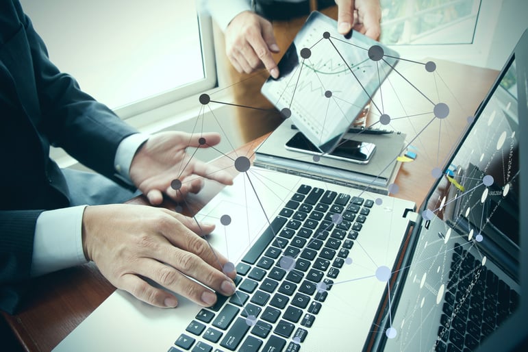 business documents on office table with smart phone and digital tablet and stylus and two colleagues discussing data in the background